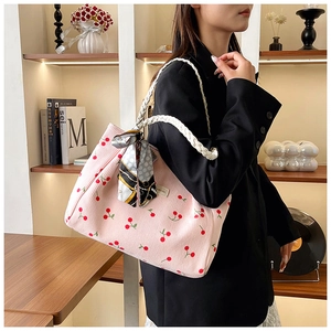 Pink corduroy tote bag with red cherry print and woven rope straps in a lifestyle setting