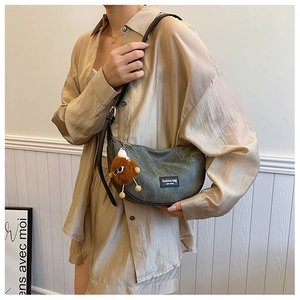 Detail of dark grey canvas half-moon bag with leather strap and plush doll pendant