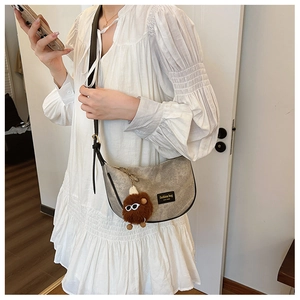 Detail of khaki crescent crossbody bag with brown pompom and black logo patch detail