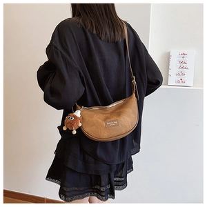 Brown faux leather crescent bag with furry monster charm shown on model in a casual outfit
