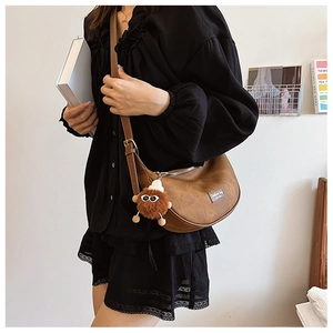 Brown semi-circle crossbody bag with fuzzy monster pendant and leather strap