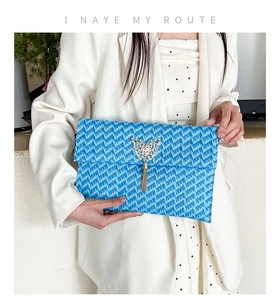 Detail of blue woven straw envelope clutch featuring a gold butterfly and fringe tassel