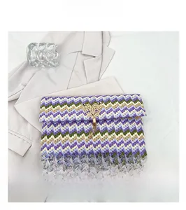 Detail of woven straw envelope clutch featuring golden butterfly clasp and metallic tassels