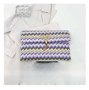 Detail of woven straw envelope bag with colorful wavy patterns and golden butterfly tassel