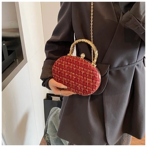 Detail of red tweed clutch bag with golden metal handle and chain on dark blazer