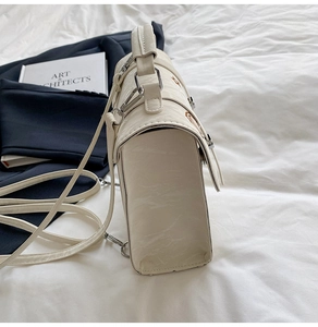 Side view of cream retro crossbody bag with accordion structure and silver buckles
