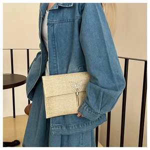 Detail of straw envelope clutch with gold butterfly clasp and metallic tassel accents