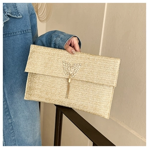 Detail of straw envelope clutch with golden butterfly charm and long hanging tassels