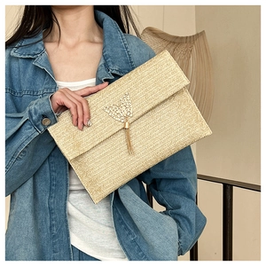 Detail view of woven straw envelope clutch with metal butterfly tassel decoration