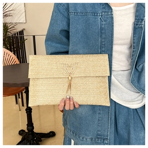 Detail of straw woven envelope clutch with metal butterfly tassel decoration