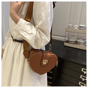 Detail of a brown heart-shaped crossbody bag with quilted lines and a golden twist lock