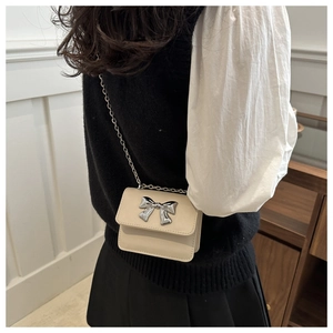 Detailed view of a beige mini crossbody bag with a silver metallic bow and chain strap