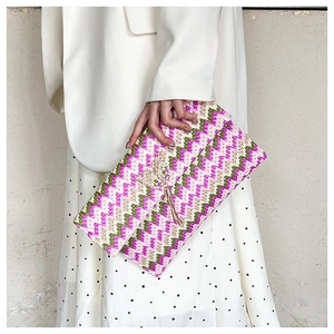 Detail of straw woven envelope clutch with pink zigzag pattern and metal butterfly tassel