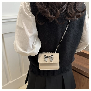 Detail view of mini crossbody bag featuring a silver bow accent and metal chain strap