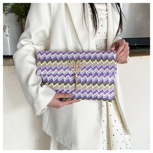 Detail of woven straw envelope clutch with purple wave patterns and a gold butterfly tassel