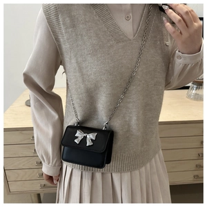 Close-up of black mini crossbody bag with silver bow accent and delicate chain strap