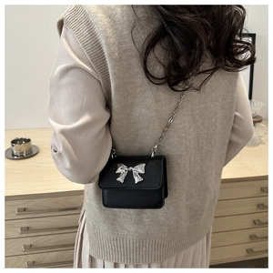 Detail of a mini black crossbody chain bag featuring a metallic silver bow on matte leather