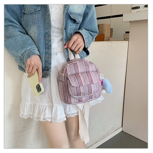 Close-up of mini striped canvas backpack with heart charm on denim jacket