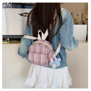 Detail of a mini striped woven backpack with plush star charm on model's back