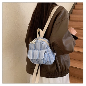 Detailed back view of a mini blue and white striped canvas backpack worn by a model