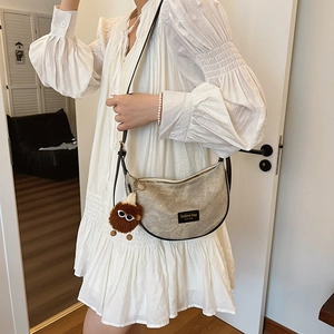 Minimalist beige crescent crossbody bag with black trim and plush doll accessory