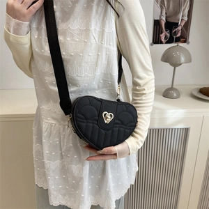Black quilted heart-shaped crossbody bag with gold lock and wide strap on model