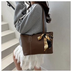 Close-up of brown faux leather tote bag with contrast stitching and decorative silk scarf
