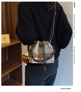 Detail view of plaid wool bucket bag featuring brown leather drawstring and plush charm