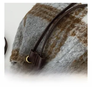 Detail of plaid tweed bucket bag with dark brown leather drawstring and golden metal eyelets