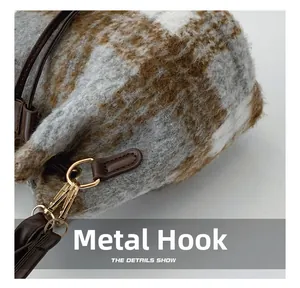 Detailed close-up of golden hardware hooks and brown leather straps on a plaid wool bag