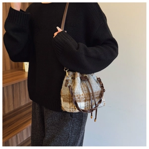 Detailed view of the plaid wool bucket bag with woven handle and leather drawstring closure
