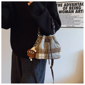 Detail of checkered tweed bucket bag with drawstring closure and brown plush pendant