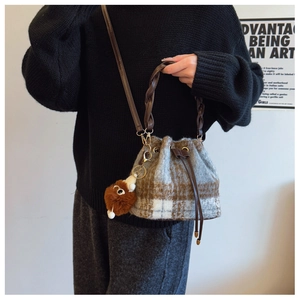 Detail of plaid wool bucket bag featuring woven leather handle and plush ball charm