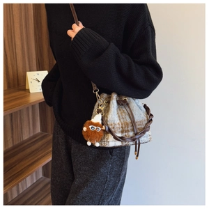 Detail of tweed bucket bag with woven handle and plush monster charm on model