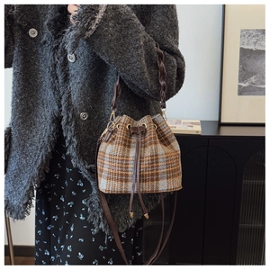 Detail of plaid bucket bag with drawstring closure and braided handle on wool coat
