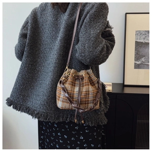 Detail of woven brown leather handle and tweed plaid pattern on drawstring bucket bag