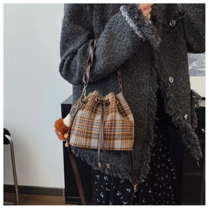 Detail view of plaid wool bucket bag with drawstring closure and plush pendant charm