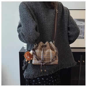 Detail of plaid bucket bag with leather strap and decorative plush ball charm