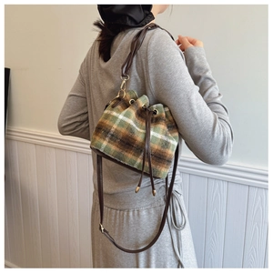 Detail of wool plaid bucket bag with brown leather strap and golden metallic buckle