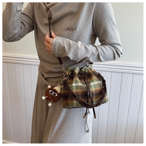 Detail of plaid tweed bucket bag featuring a brown plush doll charm and woven handle