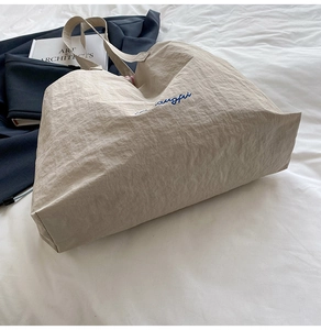Détail d'un grand cabas beige avec broderie bleue sur tissu texturé sur un lit blanc