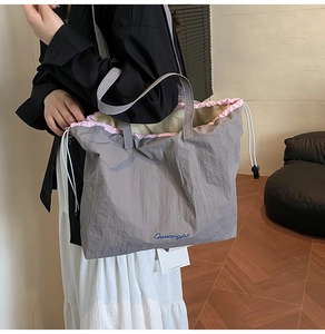 Detail of grey taupe tote bag showing pink drawstring closure and blue logo print