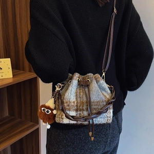 Chic checkered tweed bucket bag with braided handle and plush charm on woman's shoulder