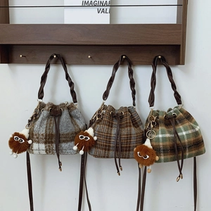 Three plaid wool bucket bags in grey, brown, and green with plush charms and woven handles