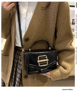 Detail of glossy black patent leather bag featuring a large gold buckle and handle