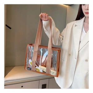 Macro shot of large transparent PVC tote with brown leather trim and woven handles