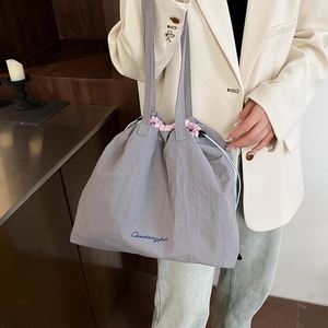Minimalist grey nylon drawstring tote bag with pink accents shown on a model for daily use