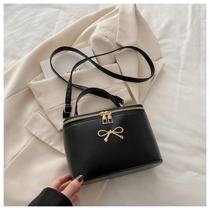 Detail of a black box-shaped handbag featuring a gold metal bow and dual zippers on a suit