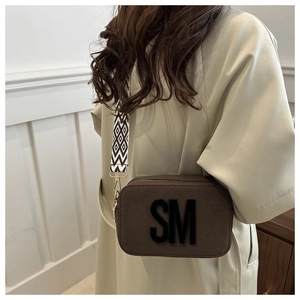 Macro view of brown suede camera bag with SM logo and geometric woven shoulder strap