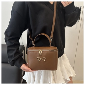 Detailed view of brown box bag featuring golden bow detail and smooth faux leather
